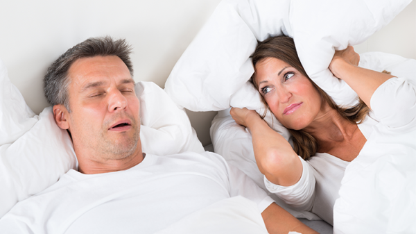 Man snoring, woman covering ears with a pillow | SleepTest.co.uk