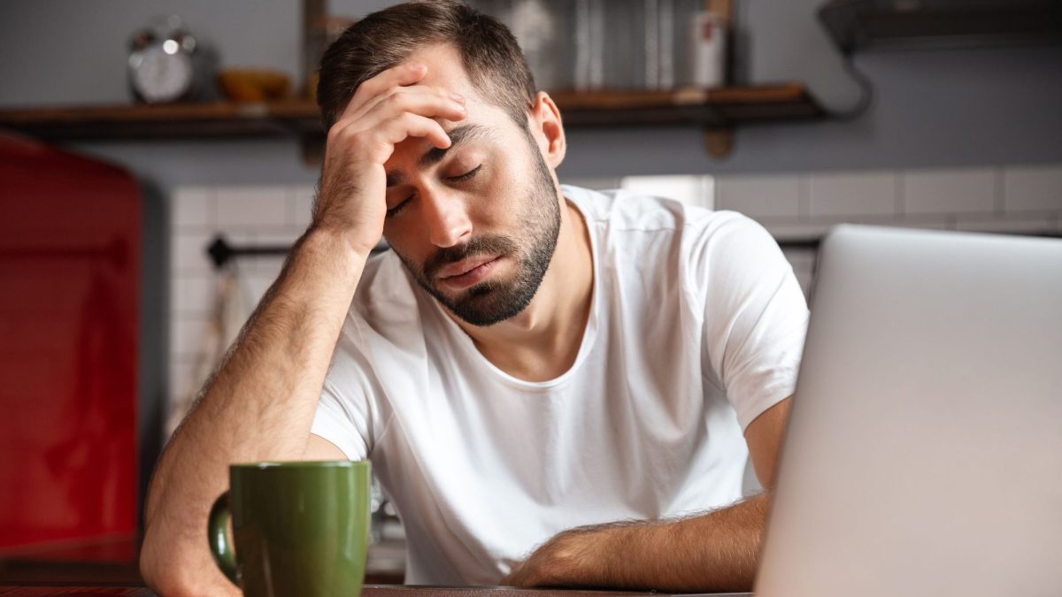 Man tired at his desk, holding his head | Sleeptest.co.uk